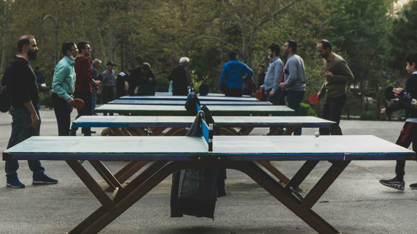 People play table tennis at outdoor park tables.
