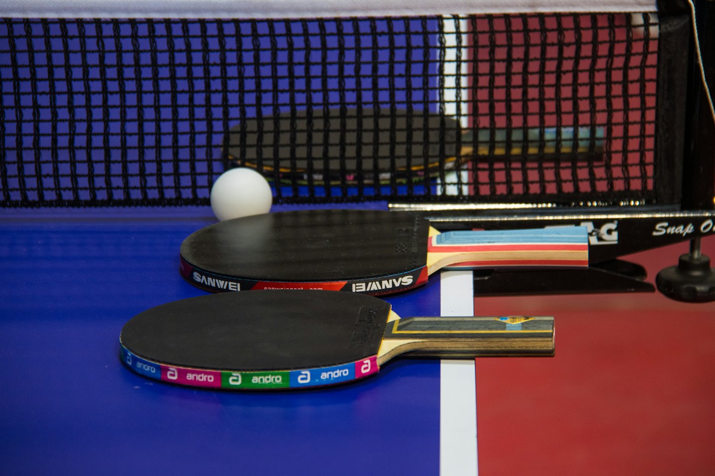 Two ping pong paddles and a ball on a table.