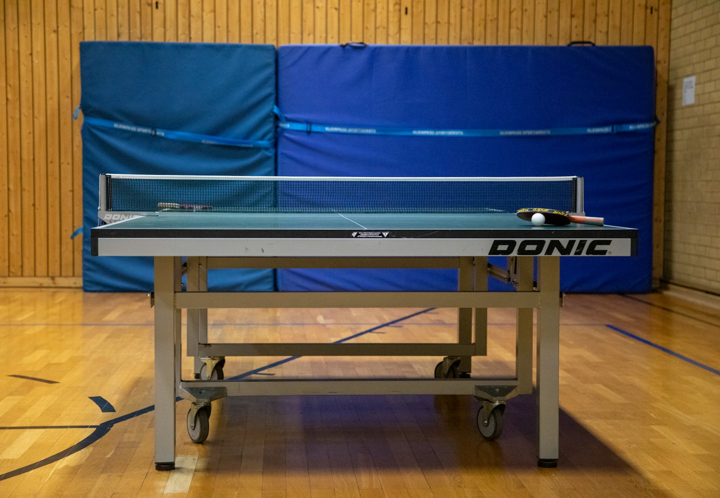 Ping pong table with paddles and ball ready for play indoors.